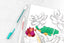 A colorful coloring book page with flowers on it and two pens next to it.