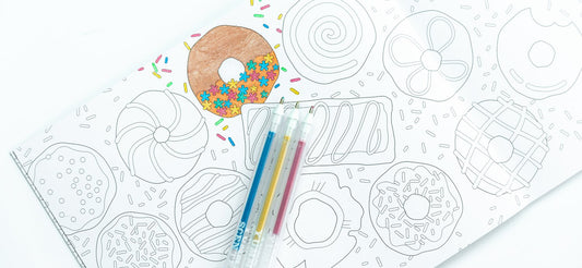 Three glitter pens lie on a coloring page of drawings of donuts.