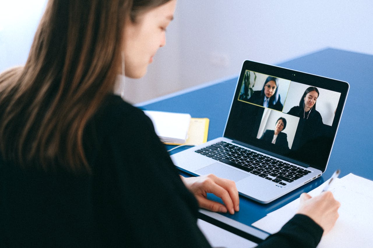 A woman at a desk doing a video call with two other people on her screen