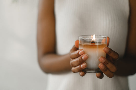 A woman in a white shirt holds a little candle in a glass jar