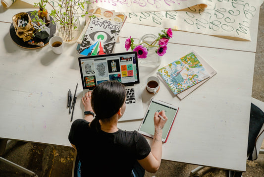 A woman works at a computer on a big white desk with magazine and pictures