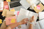 a cluttered desk with notes, notebooks, and papers and a woman's hands writing notes in a notebook