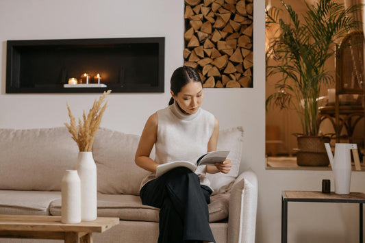 A woman looks at a magazine while sitting on a white couch in front of a fireplace