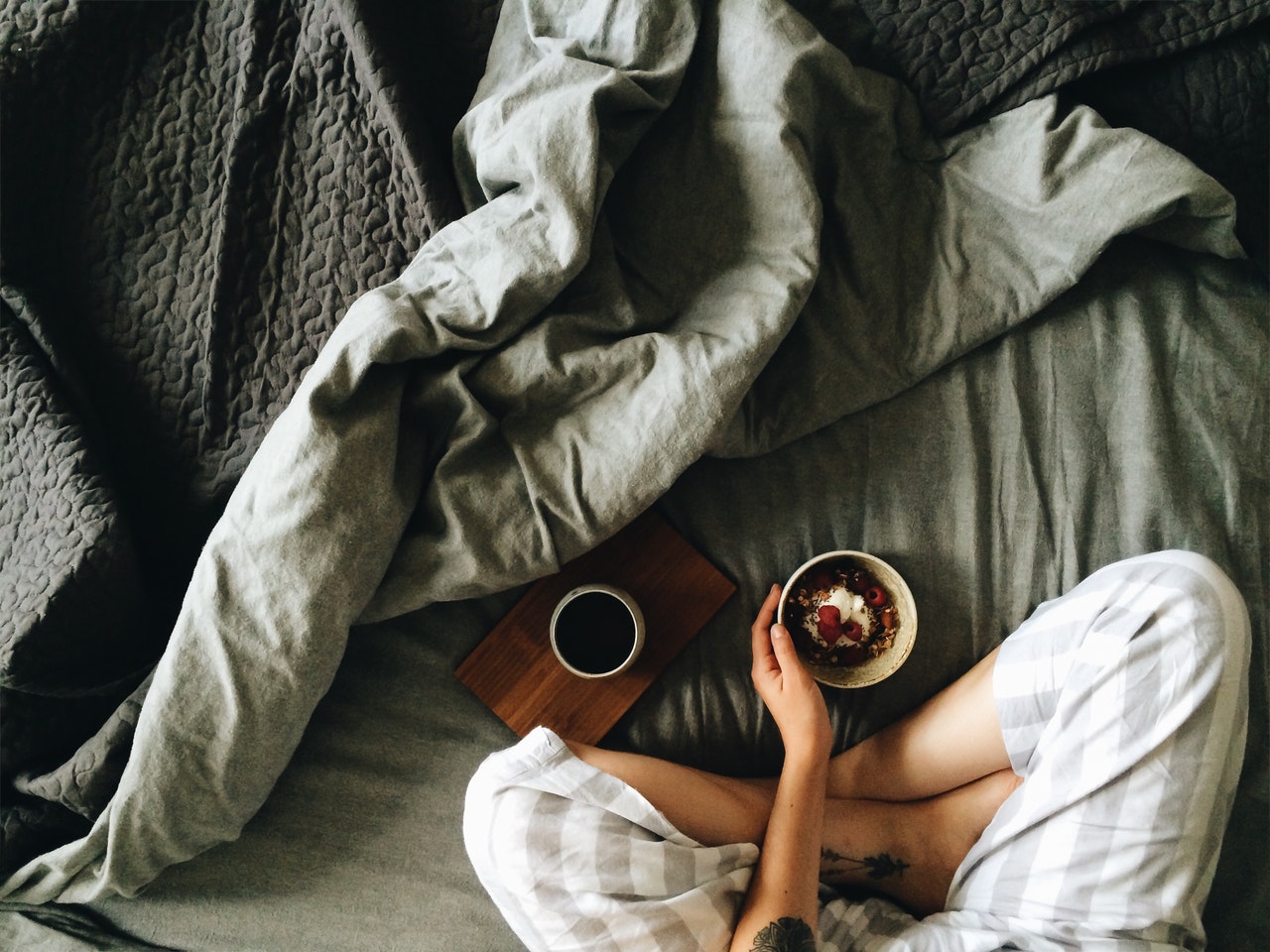 A woman sits in bed with a bowl of granola and a cup of coffee.