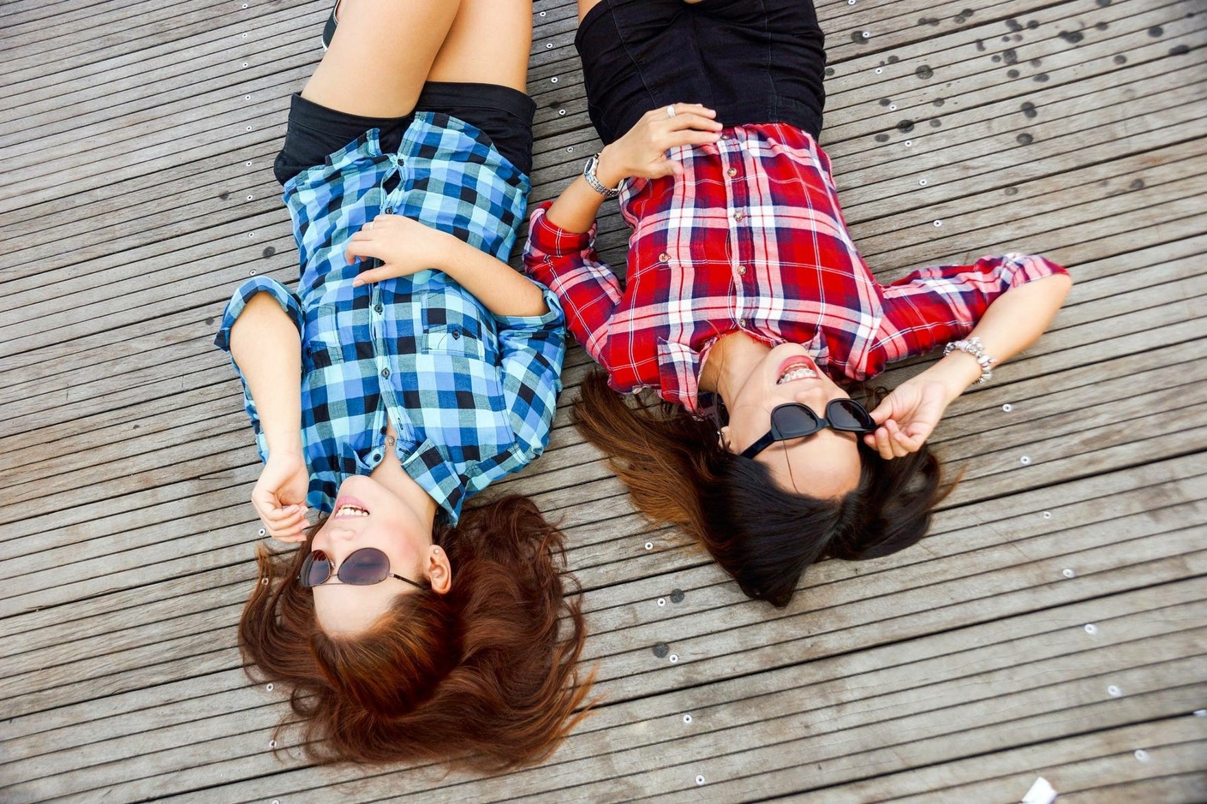 Two friends in sunglasses lie on their backs outside smiling