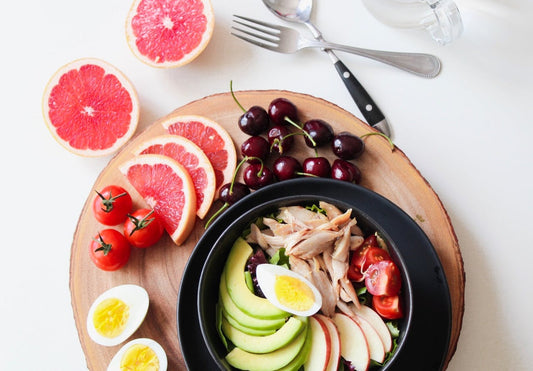 A healthy breakfast on a wooden tray with eggs, grapefruit, and avocado