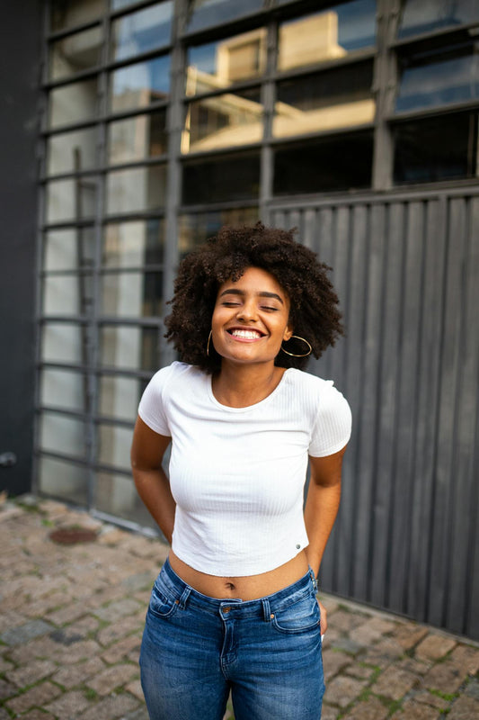 A woman in a white shirt stands outside smiling