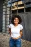 A woman in a white shirt stands outside smiling