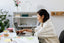 A woman sits at a white desk looking calmly at a laptop