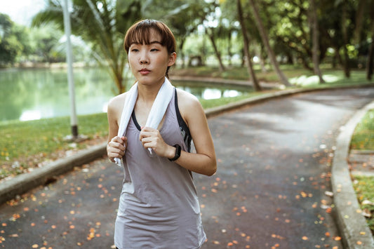 A woman walks down a park path in workout clothes with a towel over her shoulders