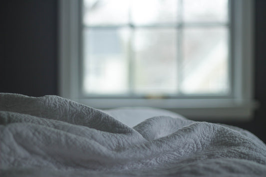 White bed linens softly stacked in front of a window