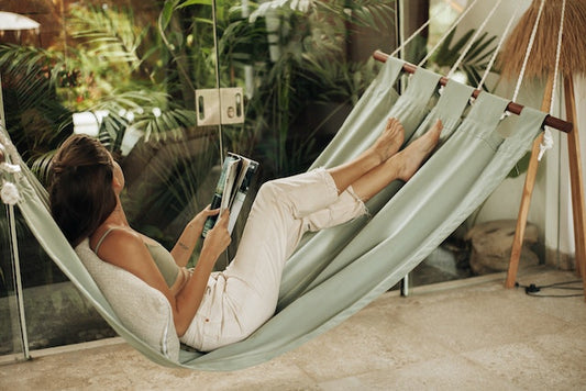 A woman in a hammock holds a magazine and looks at a window