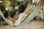 A woman in a hammock holds a magazine and looks at a window