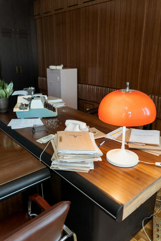 A cluttered desk with notebooks and lamps