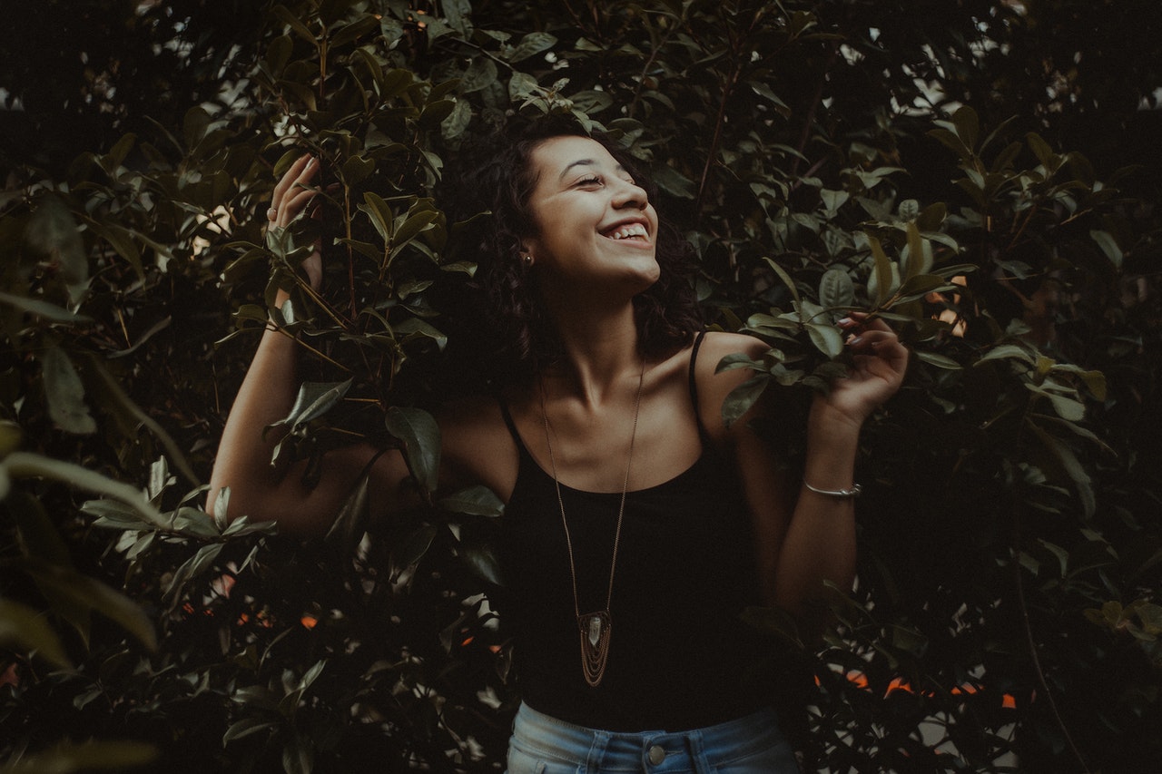 A woman smiling while holding onto leafy branches