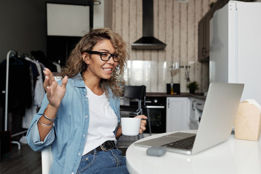 A woman holding a coffee cup looks at her laptop while having a video conversation