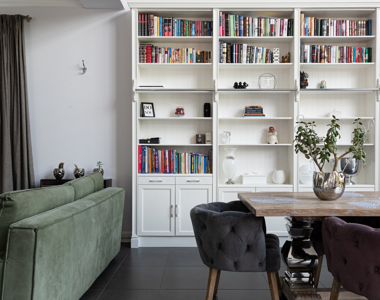 A white wall with built in bookshelves filled with books, by a green couch and wood table.