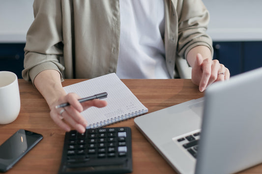 A person sits at a desk with a notebook, a calculator, and a laptop computer