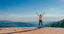 A person stands on a cliff with arms raised in the air in front of a blue sky