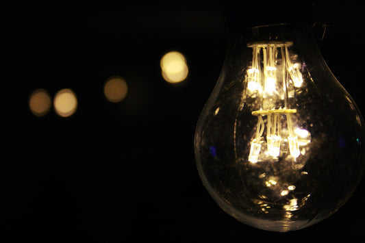 A clear lightbulb with warm light in front of a black background