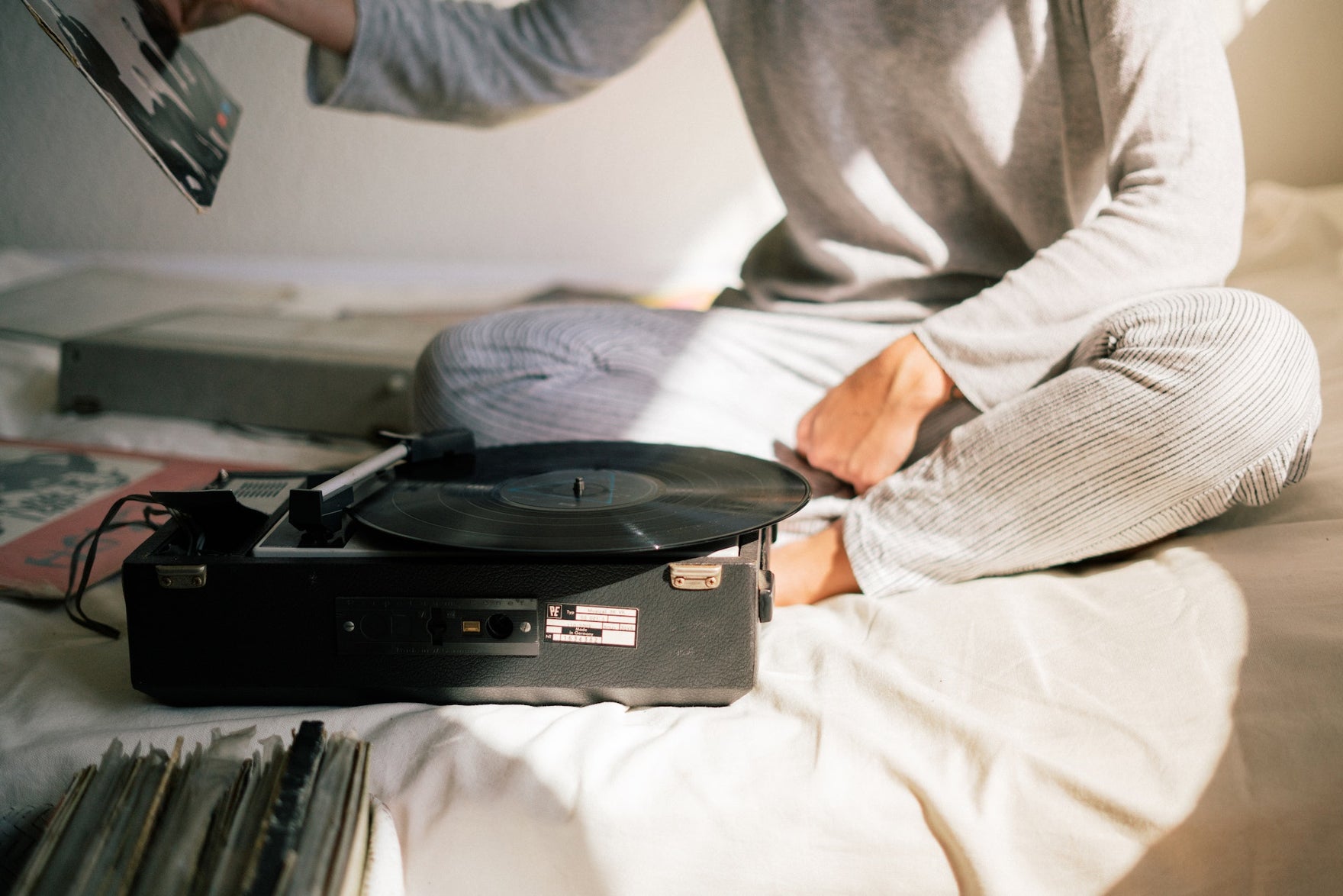 A woman sits on a bed with a record player