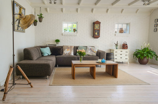 A clean house: a tidy living room with a big sofa, clean wood floors, a tidy table, and a floor plant next to a small shelf.