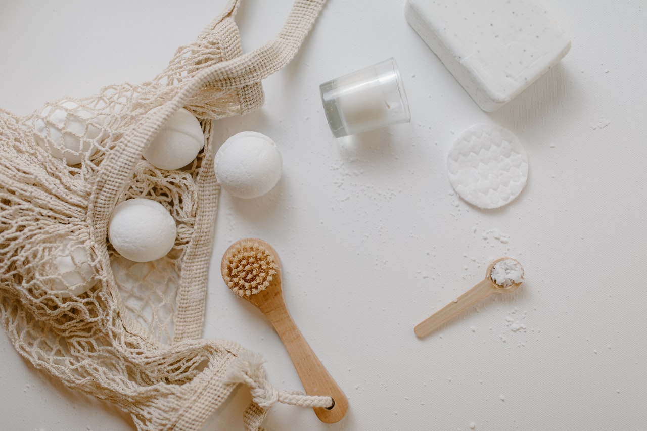 An array of white and tan self care items like scrubbers and cleansing pads on a white table