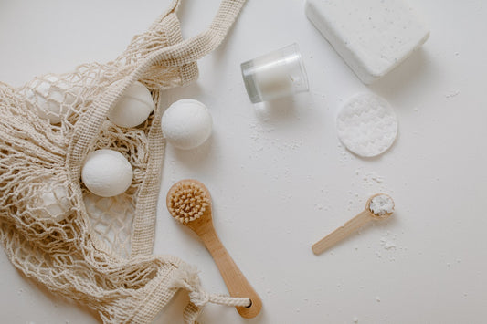 An array of white and tan self care items like scrubbers and cleansing pads on a white table