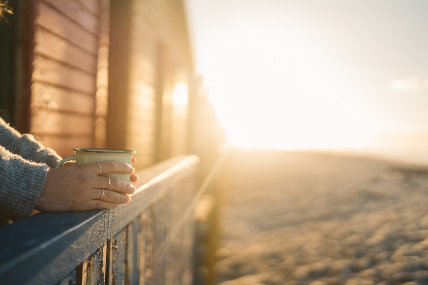 A person drinking coffee on a porch in front of morning light