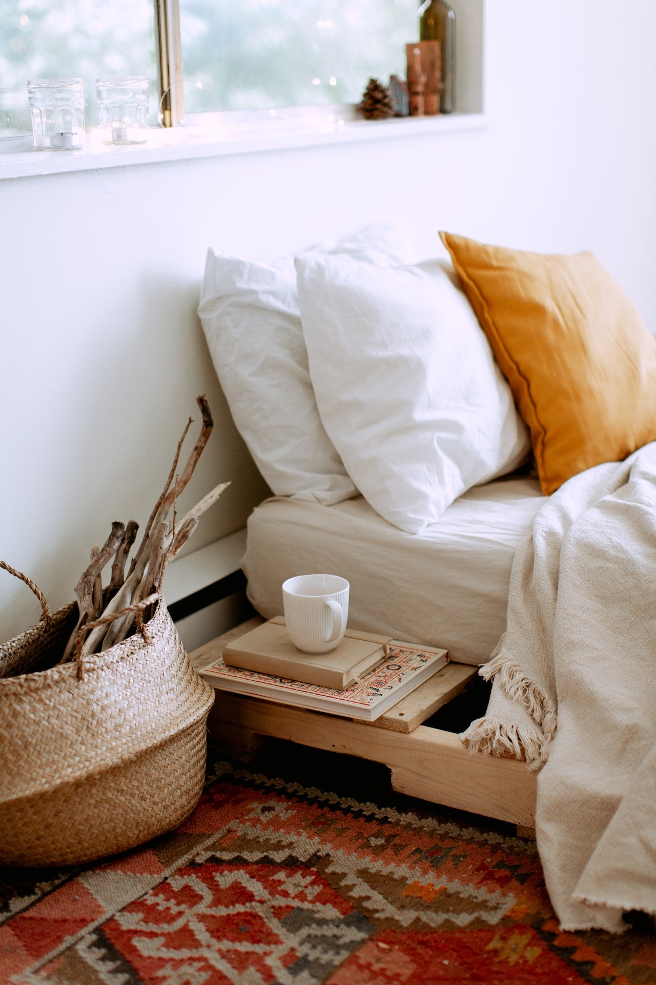 A cozy boho bed with a tea cup and a basket of sticks next to it.