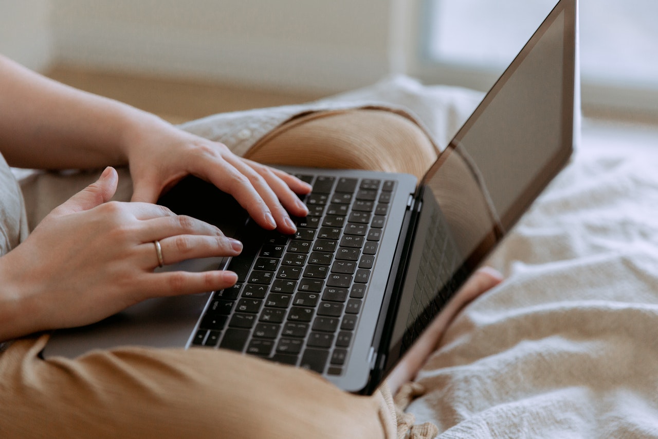 A woman sits with a laptop in her lap, the photo shows her hands typing.