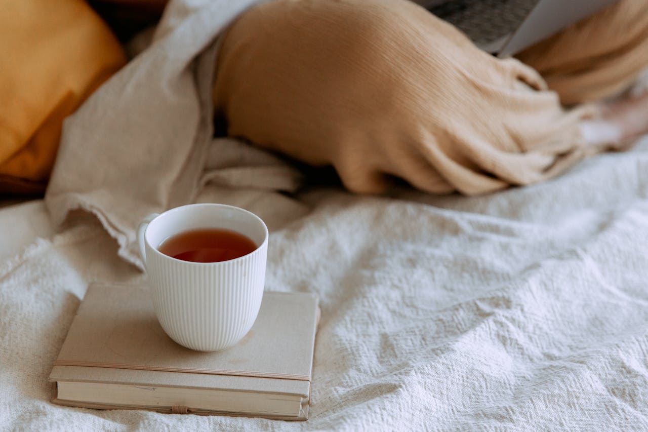 A cup of tea on a book next to a person's legs
