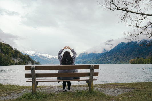 A woman sits on a bench in front of a lake