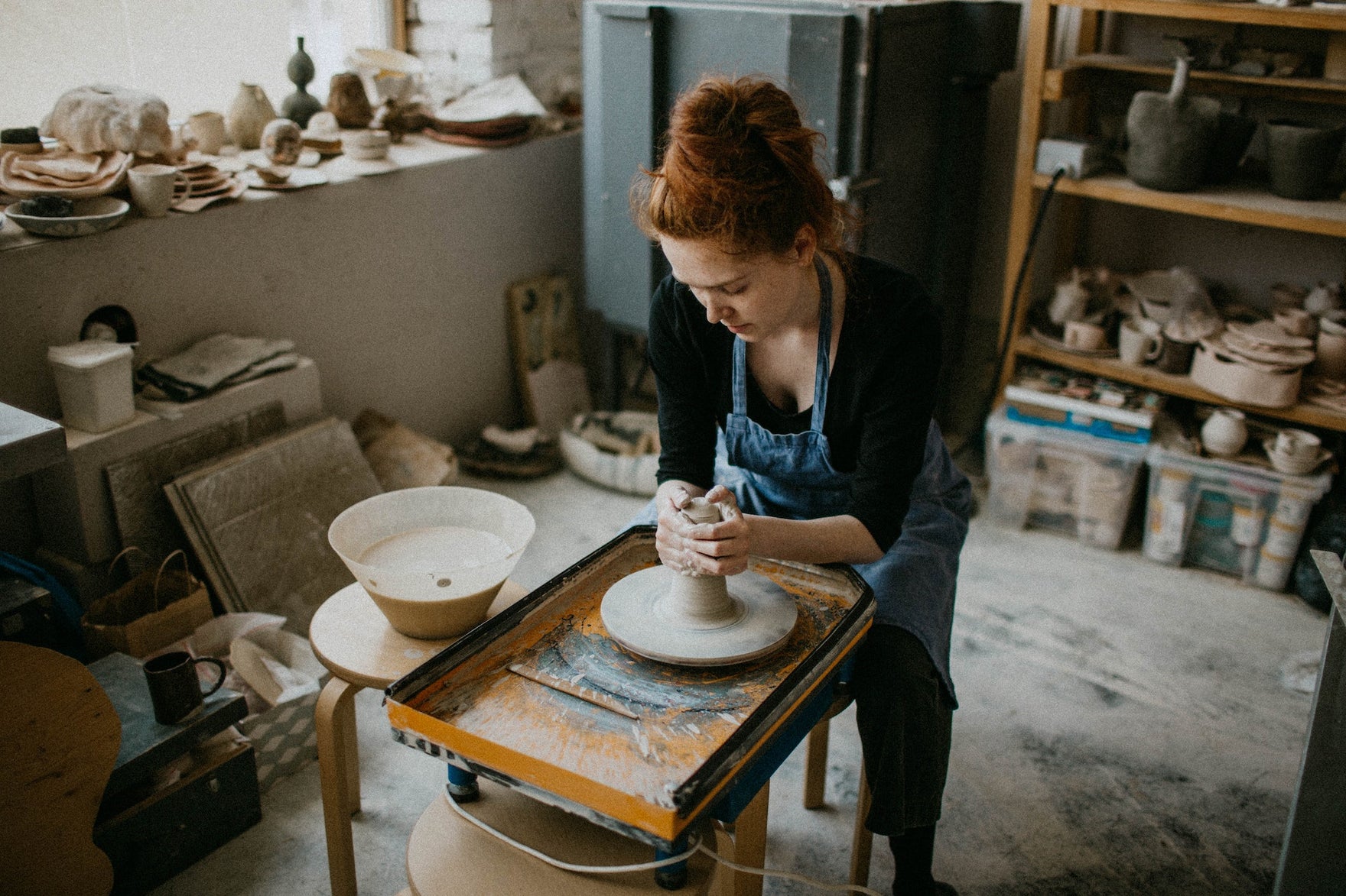 A woman works with clay on a ceramics wheel in a studio