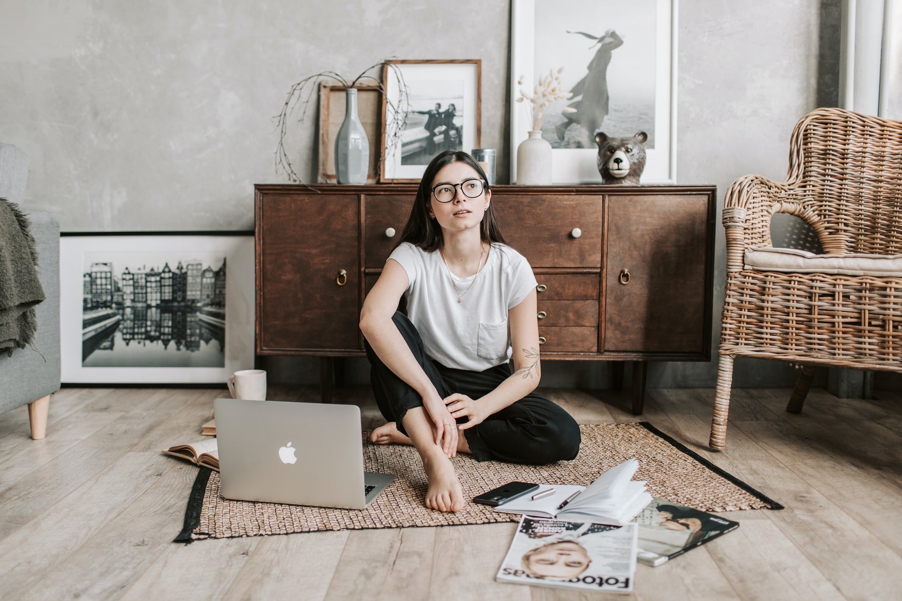 a woman sits on the floor with a computer and looks off into the distance