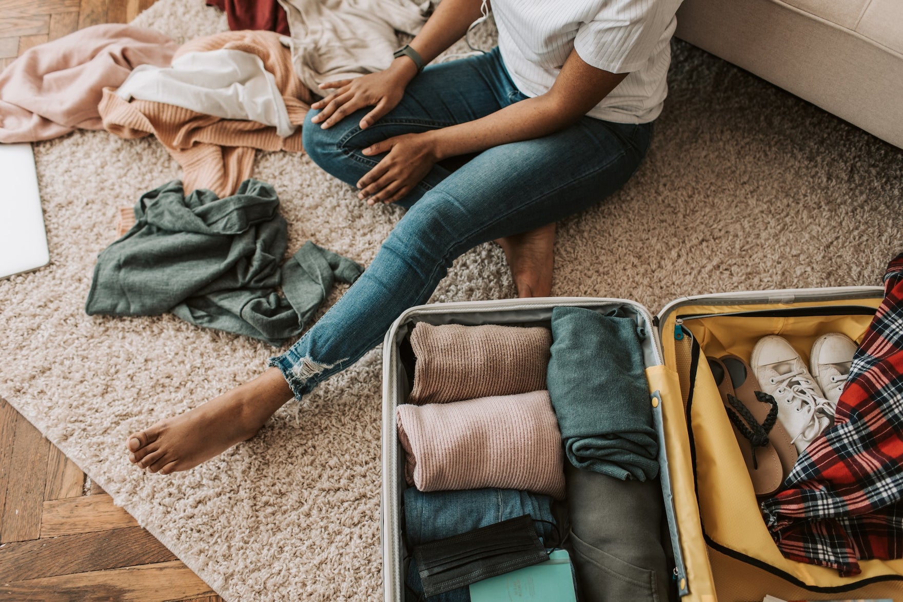 A person in jeans and a white t-shirt sits on the floor next to a packed suitcase