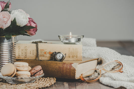 A candle on top of a stack of books next to a plate of cookies and a vase of flowers