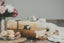 A candle on top of a stack of books next to a plate of cookies and a vase of flowers