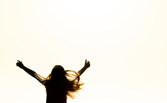 A woman in silhouette raises her arms up in a cheer.