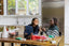 Two women sit at a kitchen table and smile at each other
