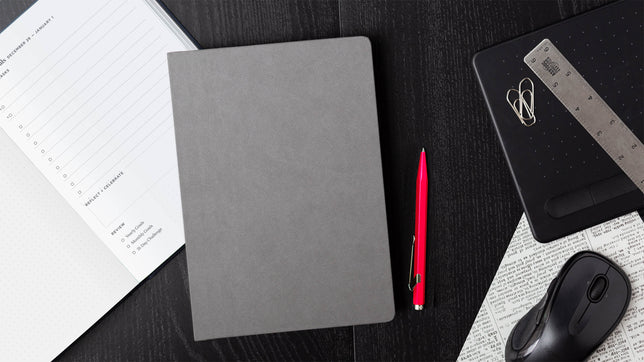 grey planner and red pen on a desk