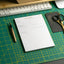 Notepad with an action plan on a green cutting mat with a keyboard and scissors in the background.