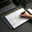 Person writing in a planner with a laptop and office supplies on a desk