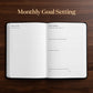 An open planner or notebook with monthly goal-setting pages displayed on a dark wood background, with the text 'Monthly Goal Setting' above it.