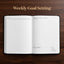 An open weekly goal-setting planner or notebook lies on a dark wood background, with the words 'Weekly Goal Setting' printed above it. The pages are white with black text and lined sections for goal tracking.