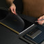 Person holding a black notebook with gold spiral binding on a dark surface.