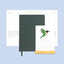 Green notebook with a stand featuring a calendar on a light blue background