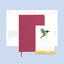 Maroon notebook with a calendar featuring a green bird illustration on a light blue background