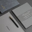 Two gray notebooks with a pen on a dark surface