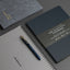 Two notebooks and a pen on a gray surface
